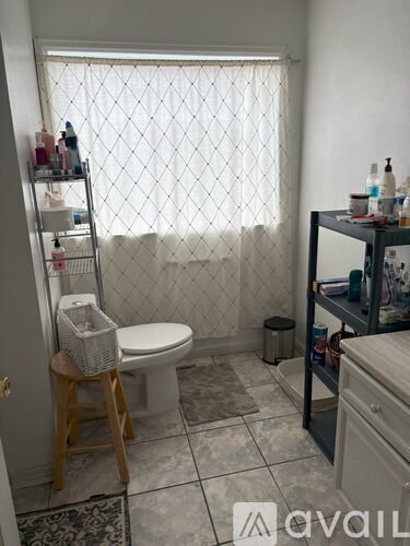 A bathroom with a toilet, sink, and a window with a curtain.
