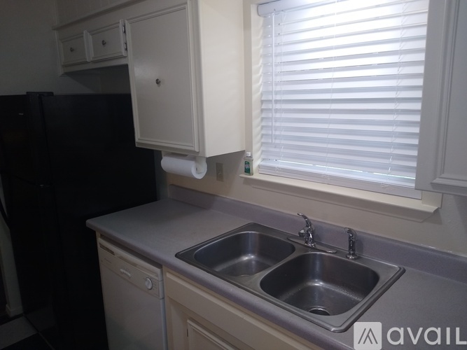 A kitchen with a black fridge, a sink with a dishwasher and a cabinet above the sink.