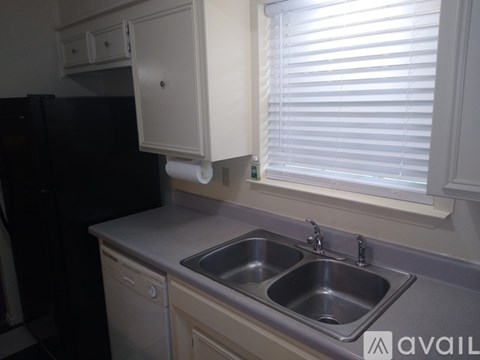 A kitchen with a black fridge, a sink with a dishwasher and a cabinet above the sink.