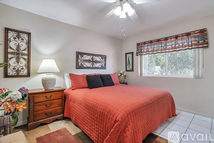 A bedroom with a red bedspread and a ceiling fan.