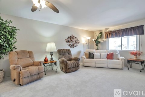 A living room with a white couch, two chairs, a table with a lamp, and a ceiling fan.