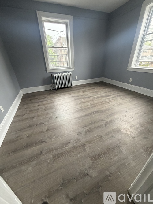 A room with grey walls and wooden flooring with a window and radiator.