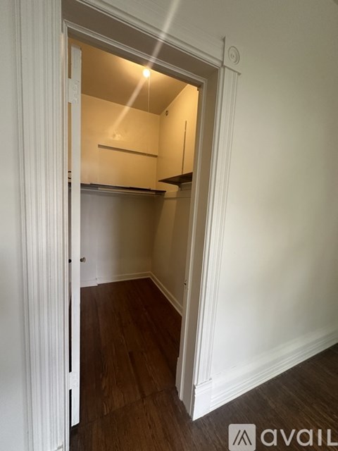 A small kitchen with white walls and wood flooring is visible through an open door.