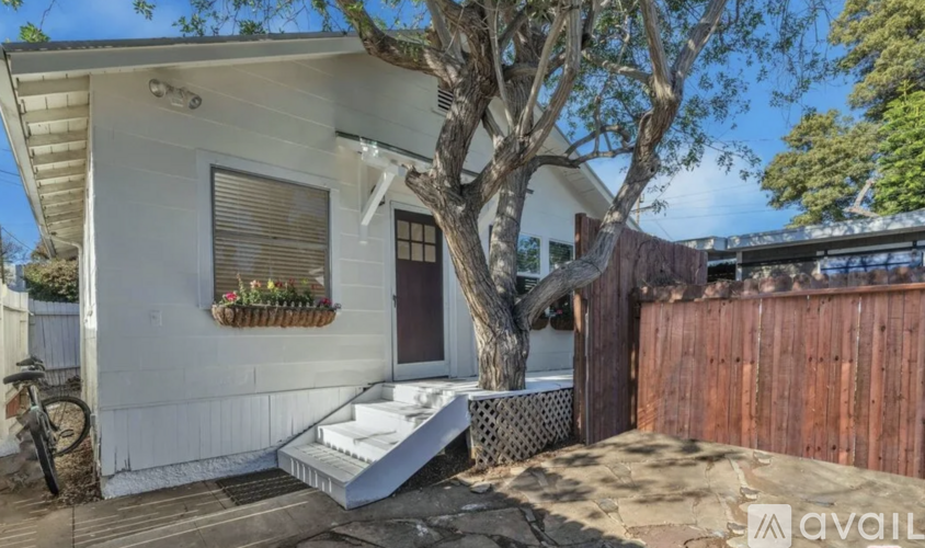 A small white house with a tree in front.
