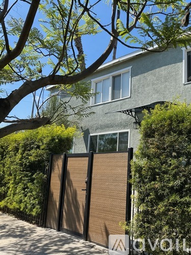 A house with a brown gate and a tree in front.