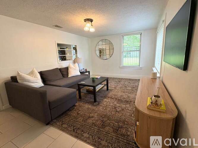 A living room with a grey couch, a coffee table, and a round window.