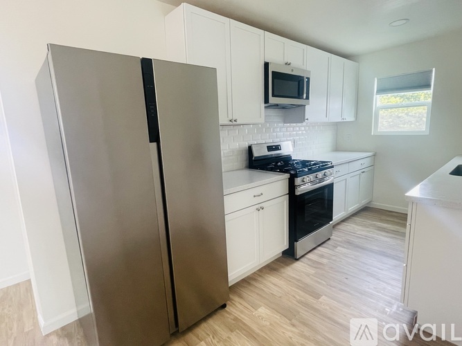A kitchen with a stainless steel refrigerator, white cabinets, and a window.