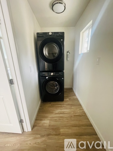 A black washer and dryer stacked on top of each other in a narrow hallway.