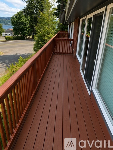 A wooden deck with a railing and a view of the street and trees.