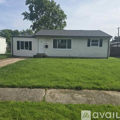 A small house with a grey roof and a white door is surrounded by a grassy area.