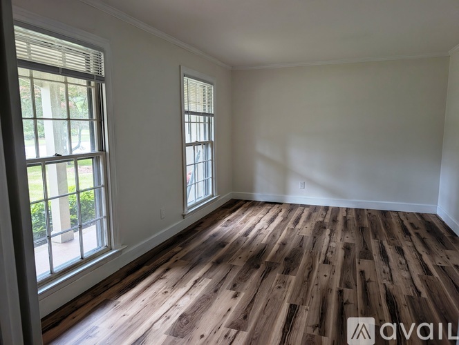 A room with wooden flooring and two windows.
