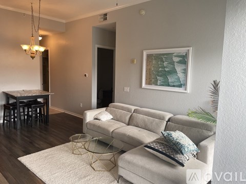 A living room with a grey couch, a white rug, and a painting on the wall.
