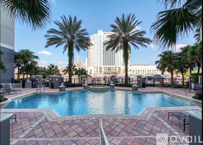 A pool surrounded by palm trees and a city skyline in the background.