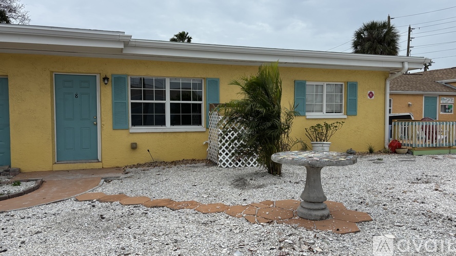 A yellow house with a blue door and a grey fountain in front.