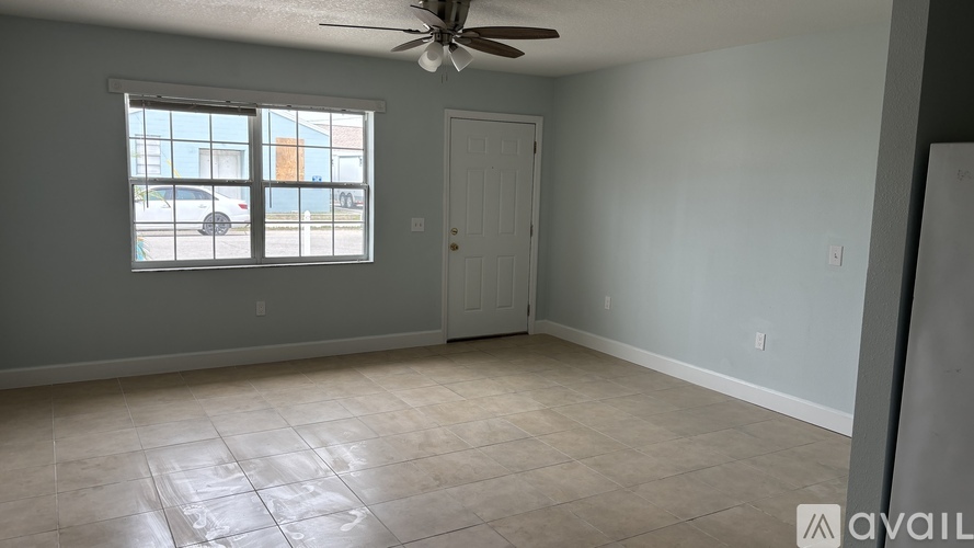 A spacious room with a ceiling fan and a window overlooking a parking lot.