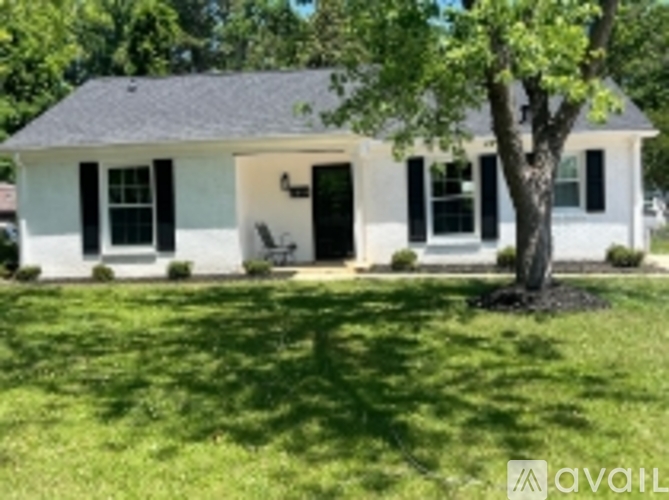 A white house with a black door and windows is surrounded by green grass.