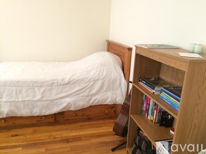 A bed with a white sheet and a wooden bookshelf with books on it.