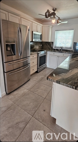 A kitchen with a stainless steel refrigerator and a marble countertop.