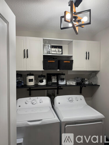 A small kitchen with two washing machines and a shelf above them.