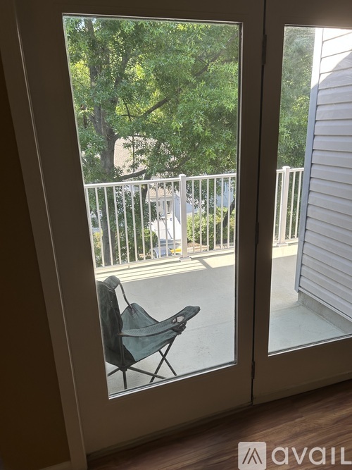 A chair is on a balcony with a view of a tree and a building.