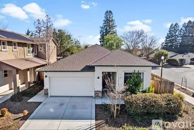 A house with a brown roof and a white garage door is surrounded by other houses and trees.