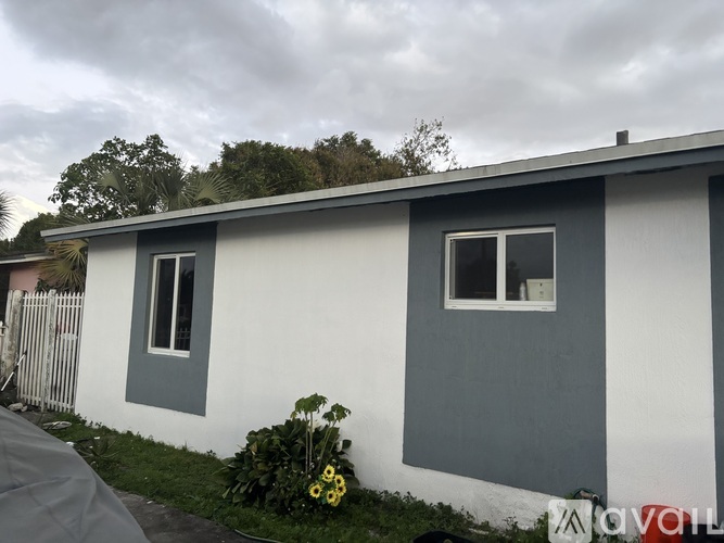 A small white house with a grey roof and a grey fence.