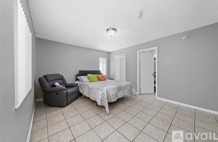 A bedroom with a bed, chair, and a window.