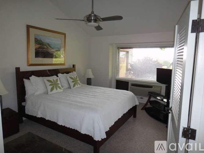 A bedroom with a bed, a ceiling fan, and a painting on the wall.