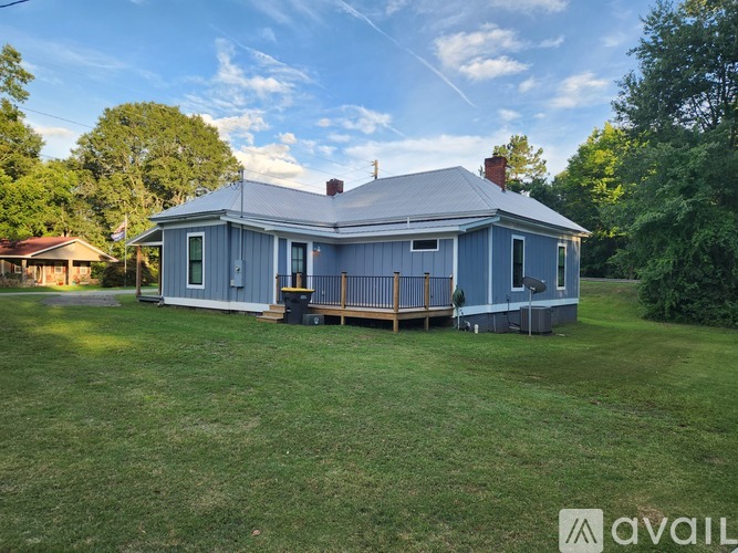 A blue house with a porch and a chimney is surrounded by a green lawn.