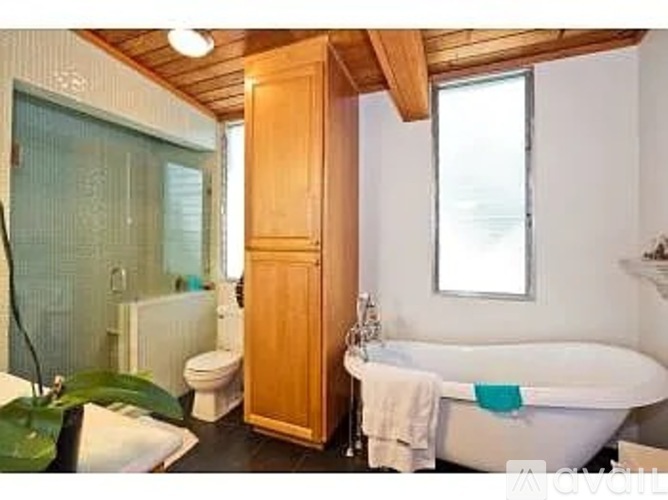 A bathroom with a wooden cabinet, a white tub, and a toilet.