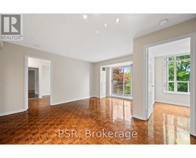 A room with wooden flooring and white walls, with a window showing greenery outside.
