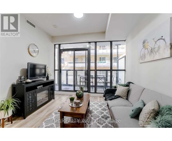 A living room with a grey couch, a wooden coffee table, a flat screen TV, and a glass door leading to a balcony.