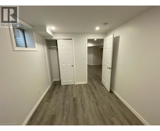 A room with white walls and wood flooring, with a window on the left wall.