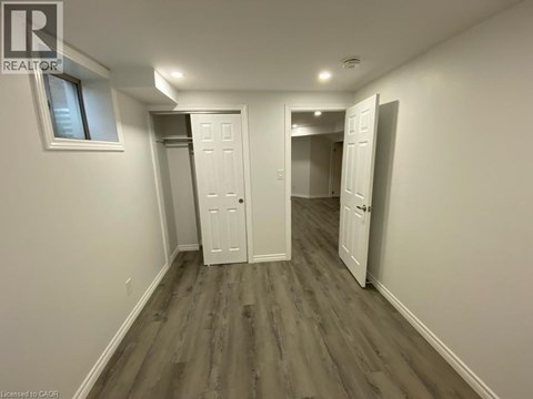 A room with white walls and wood flooring, with a window on the left wall.