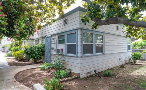 A small house with a grey siding and a red window.