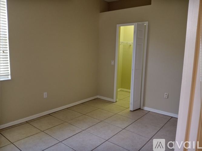 A room with beige walls and a tiled floor with a doorway leading to another room.