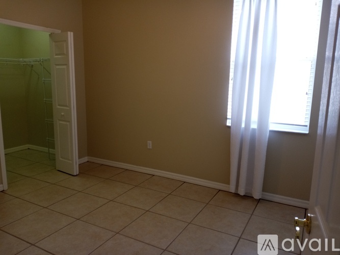 A room with beige walls and a tiled floor with a doorway leading to a bathroom.