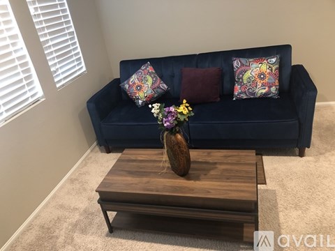 A blue couch with two patterned pillows and a vase with flowers on a wooden coffee table.