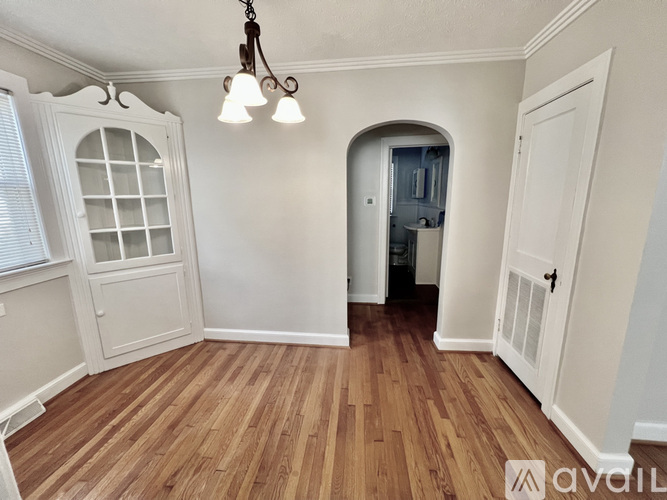 A room with wooden floors and white walls, featuring a doorway leading to another room.