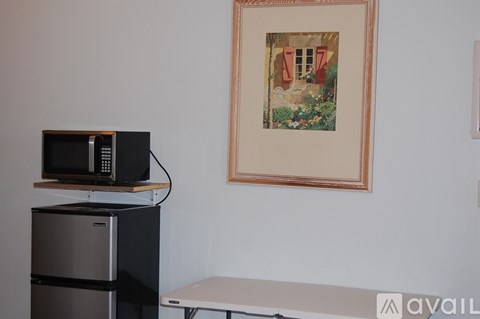 A framed picture hangs on a wall above a microwave and below a stove.