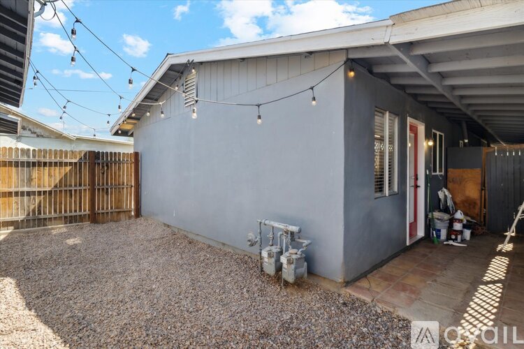 A gravel patio area with a grey building and string lights.