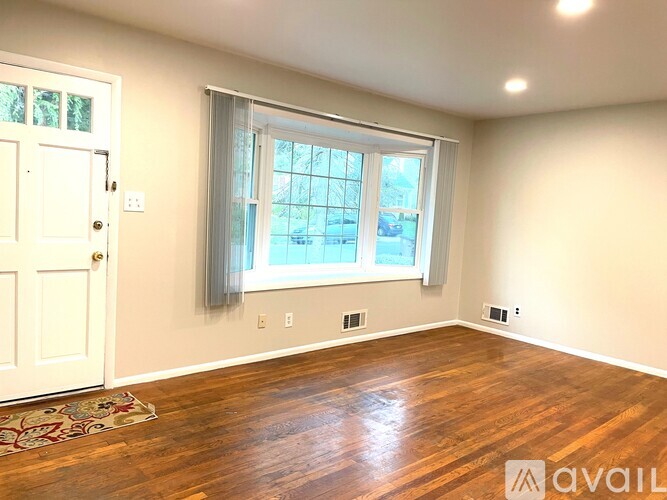 A room with a white door, a window with a grey curtain, and a wooden floor.