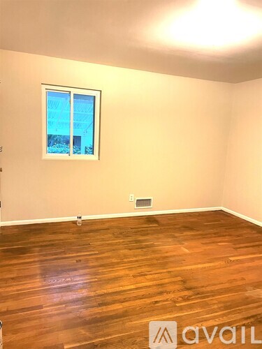 A room with wooden flooring and a window showing a view of a building.