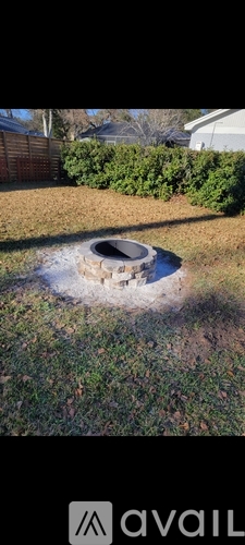 A backyard with a fire pit surrounded by grass and bushes.