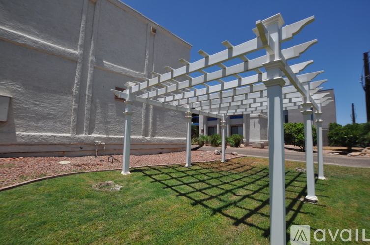 A white pergola is situated in a grassy area in front of a building.