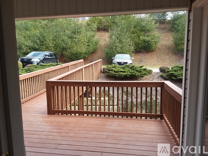 A deck with a railing and a view of a driveway with cars.