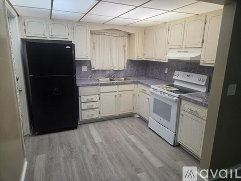 A kitchen with a black fridge, white cabinets, and a white stove top oven.