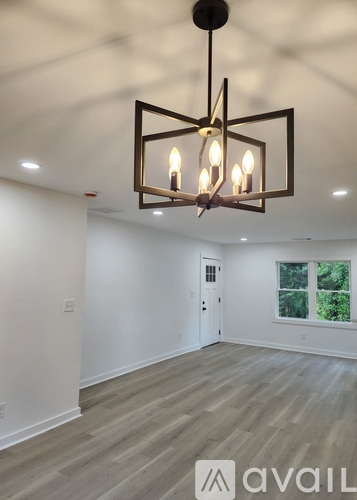 A modern chandelier hangs over a spacious room with wood flooring.