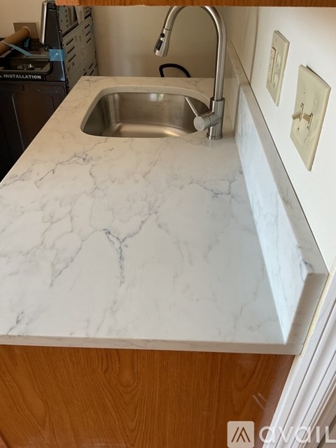 A kitchen sink with a marble countertop and wooden cabinets.