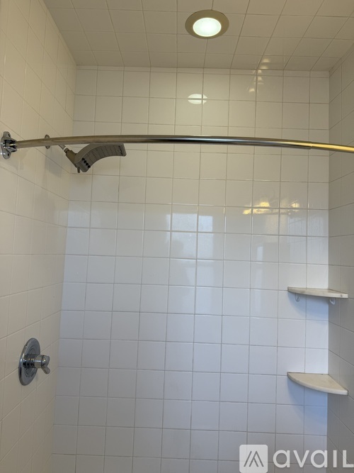 A white tiled shower area with a hand held shower head.